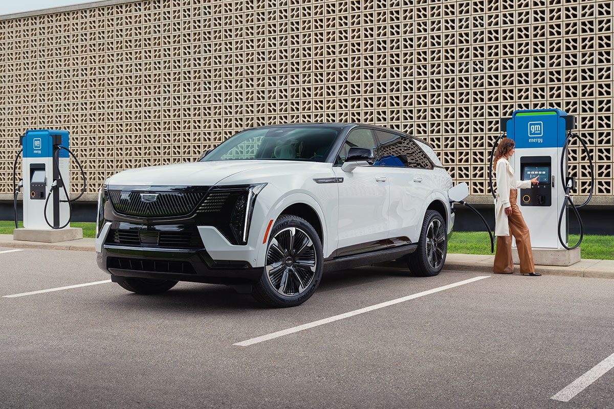 A Woman Getting Ready to Charge a Parked White Cadillac ESCALADE IQ at a GM Energy EV Charger