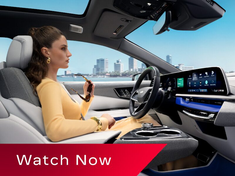 Passenger View of a Woman Driving a Cadillac OPTIQ Past the City While Utilizing Super Cruise Hands-free Technology