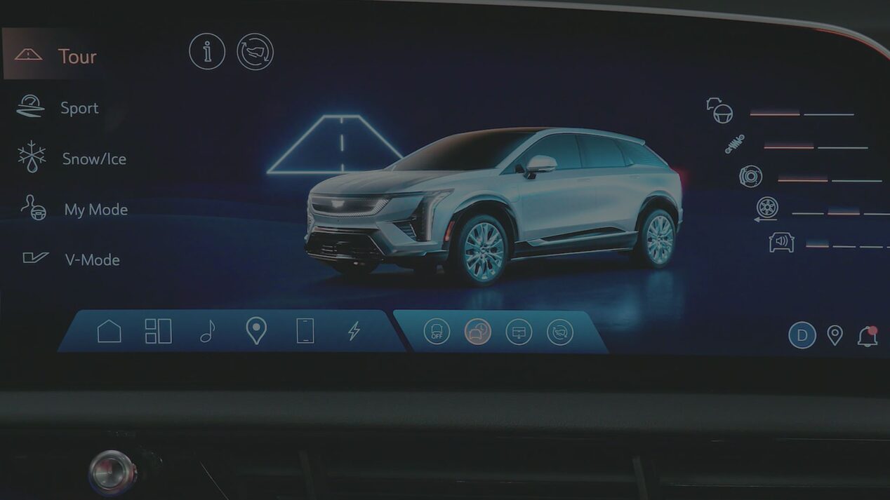A Cadillac OPTIQ Infotainment Screen Displaying Drive Mode Options Beside a Rendered Image Of a Silver Cadillac SUV.