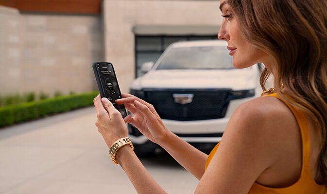 A Woman Using the Cadillac Mobile App on Her Smartphone Standing Next to Her Cadillac Vehicle