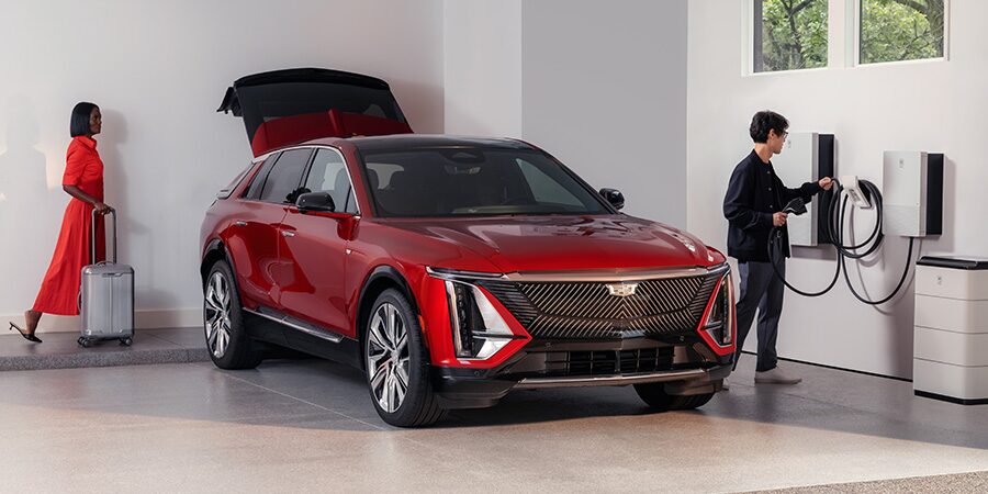 A Man Is Charging a Red Cadillac EV While a Woman is Putting the Luggage in the Trunk