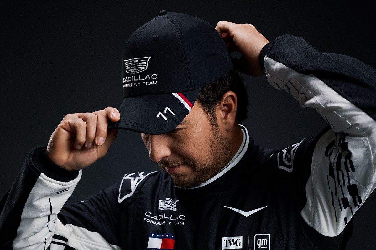 A Team Member Wearing A Black Cadillac-Branded Cap Adjusts the Brim While Posed Against A Dark Studio Background.