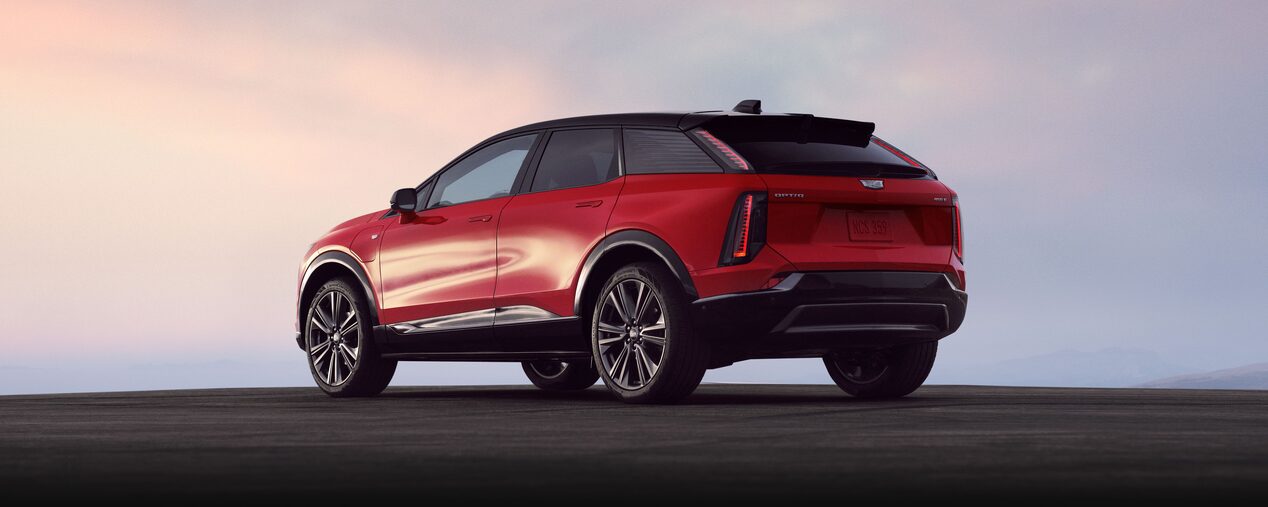 Rear Three-quarter View of a Red Cadillac OPTIQ EV SUV Outlooking a Beautiful Sky