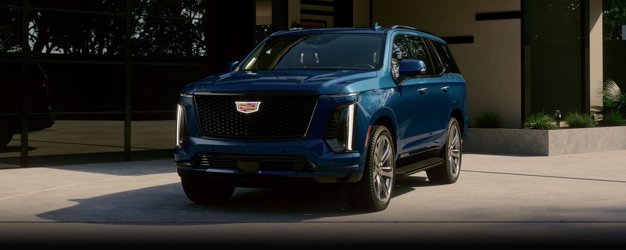 Front Three-quarters View of a Cadillac Escalade 3-row SUV Parked Outside of a Modern Home