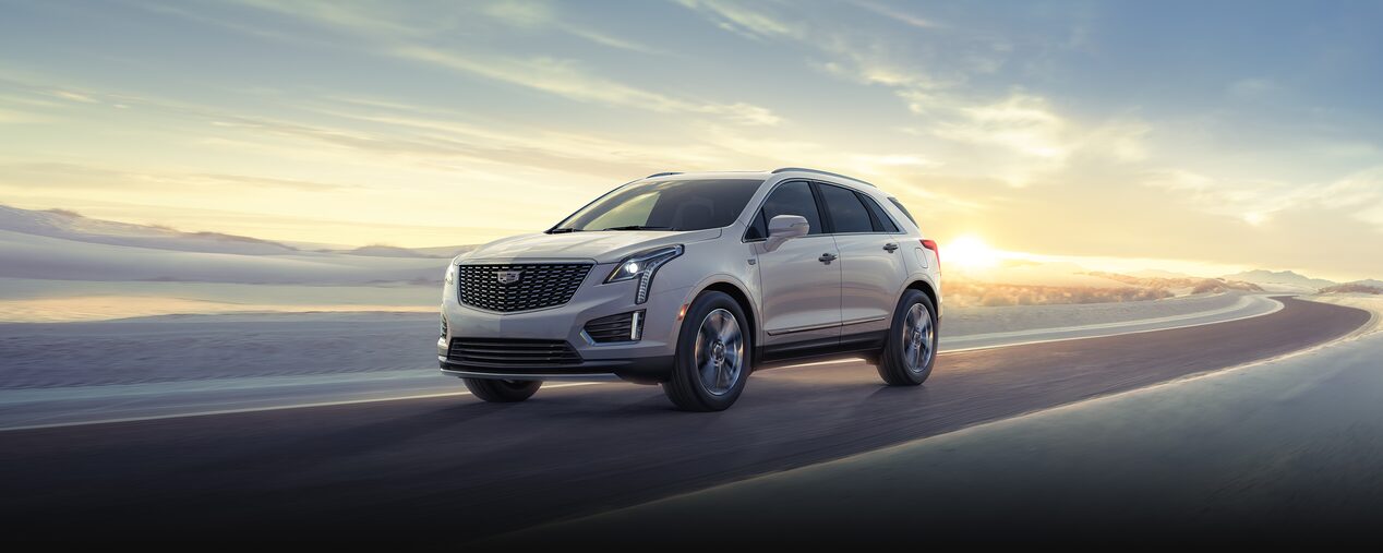 The 2025 Cadillac XT5 Driving on a Road with Sun Rising in Background