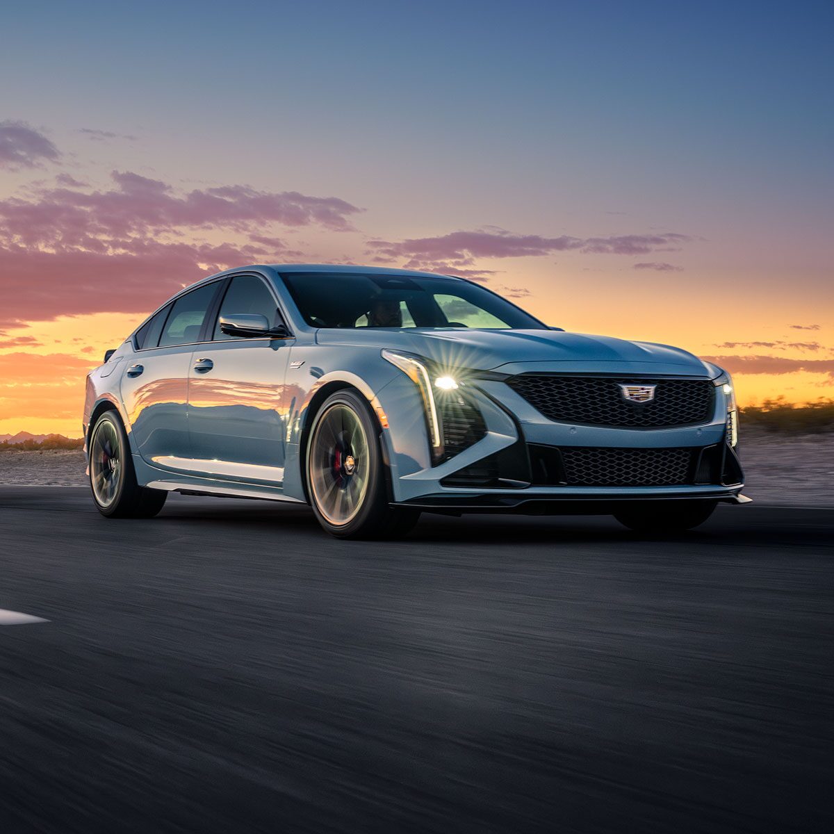 Two 2025 Cadillac CT5 V-Series Driving Down Winding Road with Stunning Sun Setting