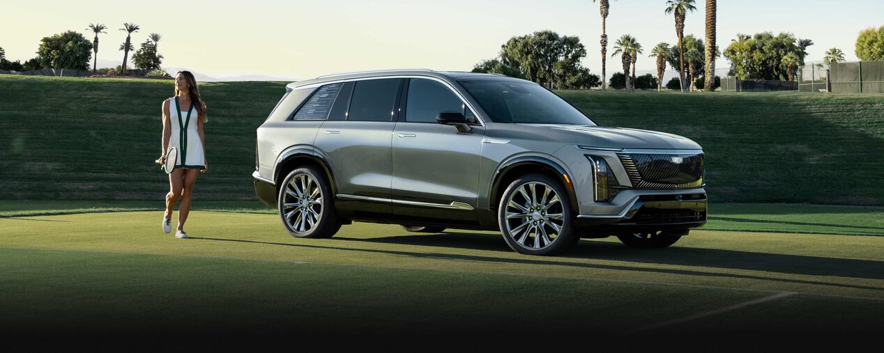 Side View of a 2026 VISTIQ Parked on a Grassy Tennis Court Next to a Tennis Player