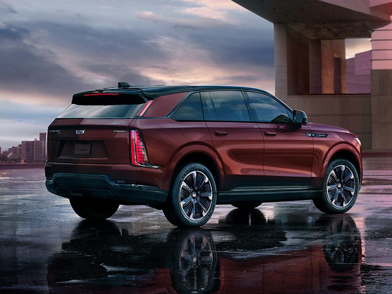 Three-quarter Rear View of a Maroon 2026 ESCALADE IQ EV SUV Parked Under its Reflection