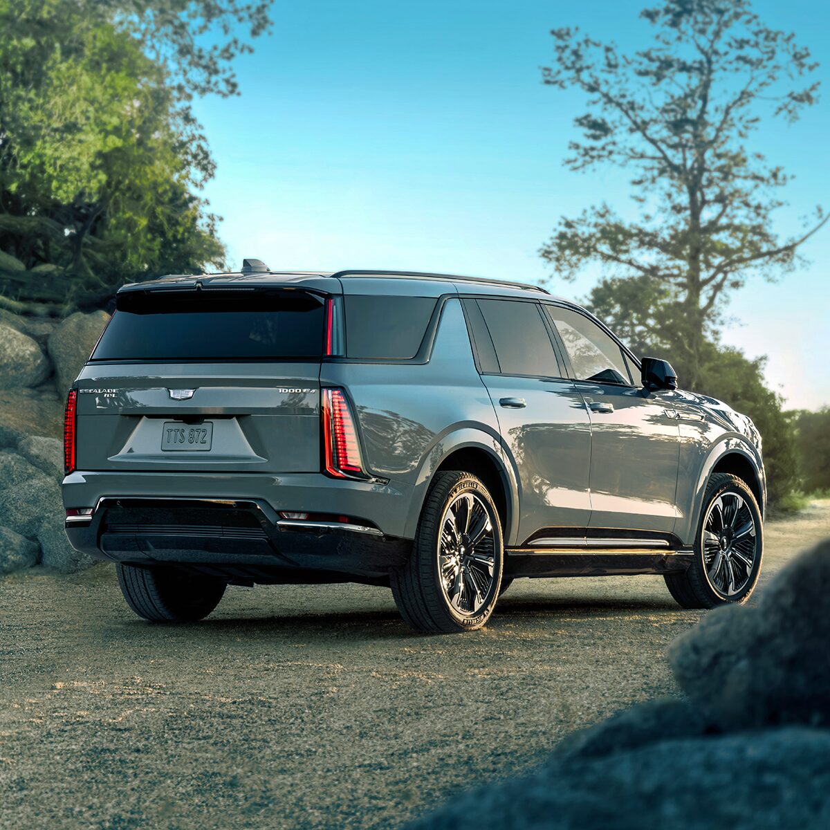 Rear Three-Quarter View of the 2026 ESCALADE IQL Parked Near a Rocky Trail