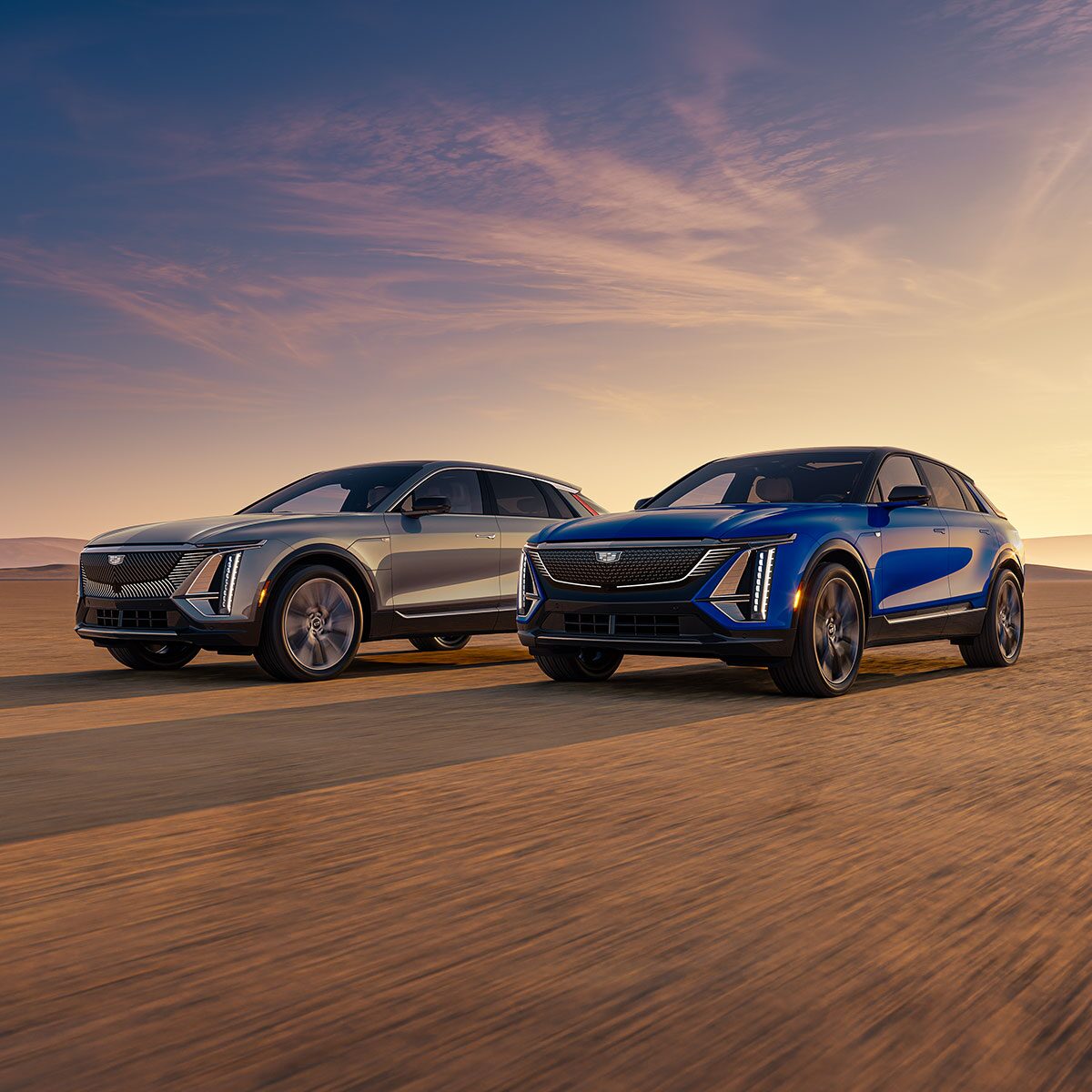 A Blue Cadillac LYRIQ and Silver LYRIQ Parked Next to Each Other in the Desert During a Sunset