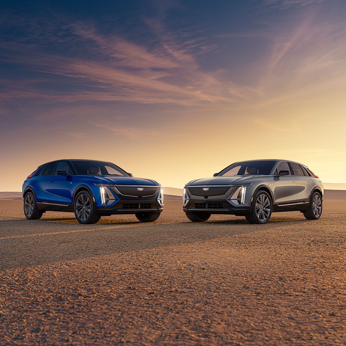 A Blue Cadillac LYRIQ and Magnus Metal LYRIQ V-Series Facing Each Other in the Desert During a Sunset