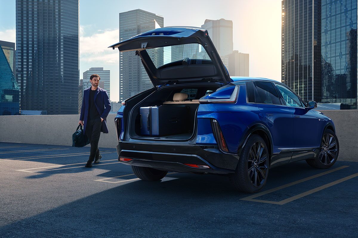 A Man Walking to an Opened Trunk of a Parked Blue Cadillac LYRIQ Outlooking the City
