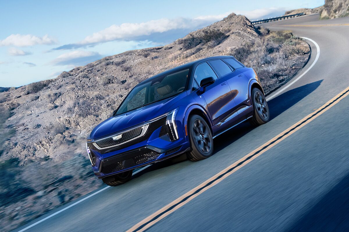 Three-quarters View of a Blue 2026 OPTIQ-V Driving Through a Mountain Road