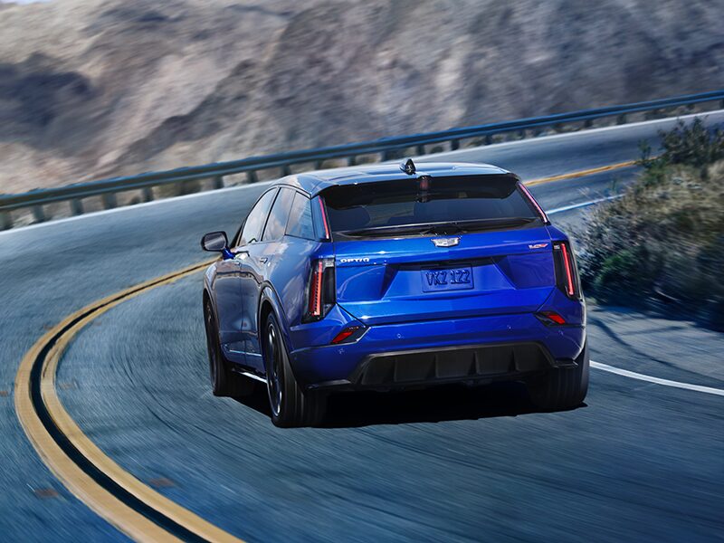 Rear View of a Blue 2026 OPTIQ-V Driving on a Curve of a Mountain Row