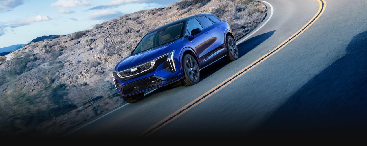 Three-quarters View of a Blue 2026 OPTIQ-V Driving Through a Mountain Road