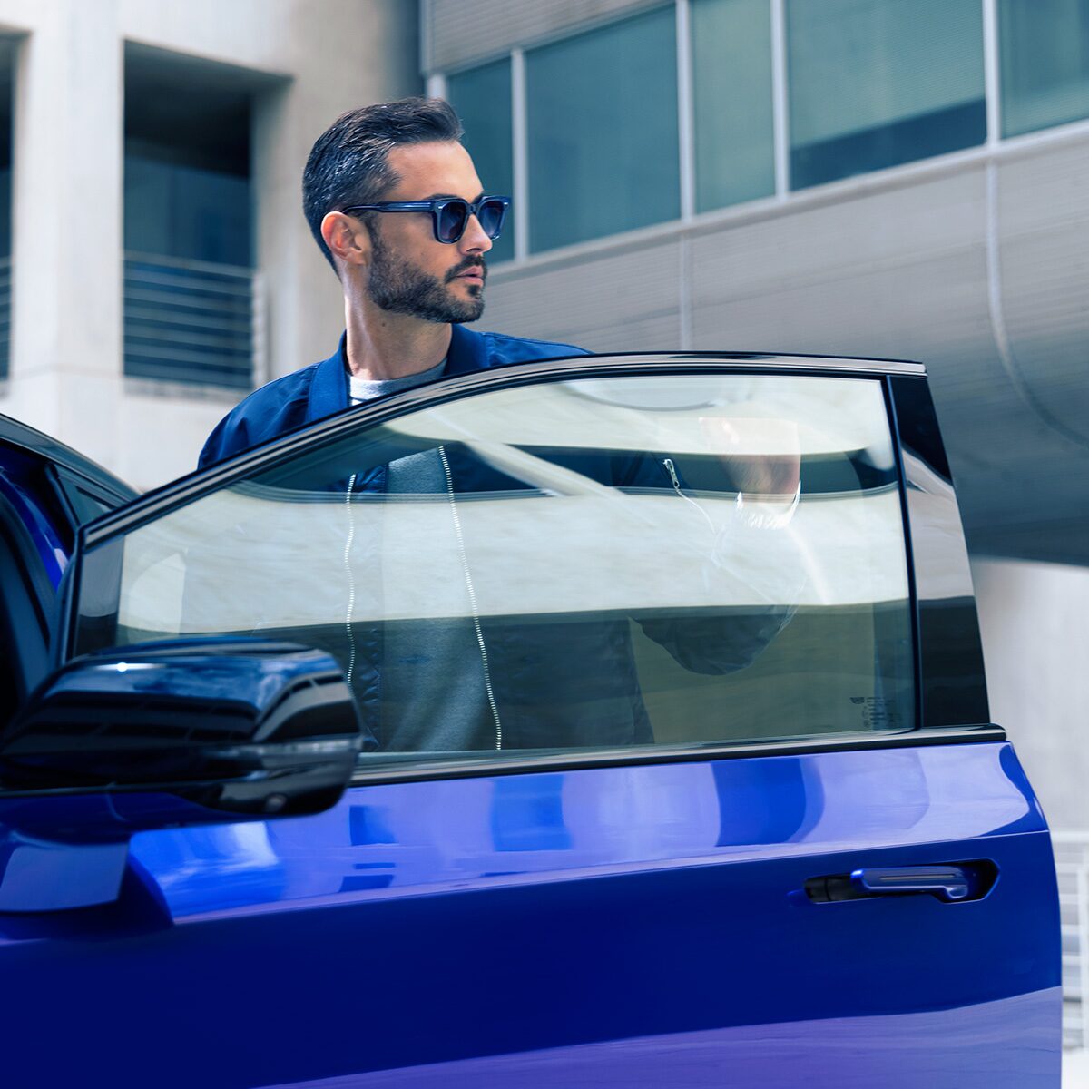 A Man in Sunglasses Standing Next to a Parked Blue 2026 OPTIQ-V