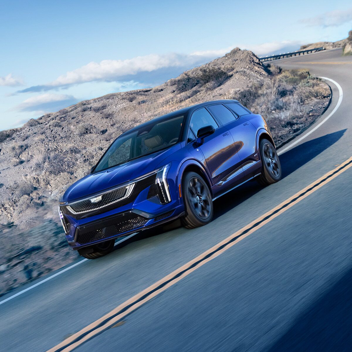 Three-quarters View of a Blue 2026 OPTIQ-V Driving Through a Mountain Road