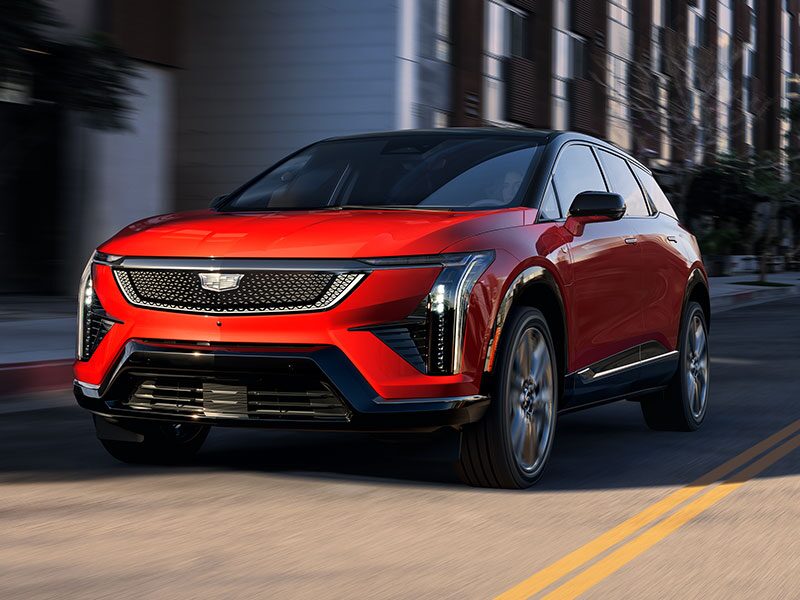 Three Quarters View of a Red Cadillac OPTIQ Driving Down the Road with Sunlight Hitting the Front of the Vehicle