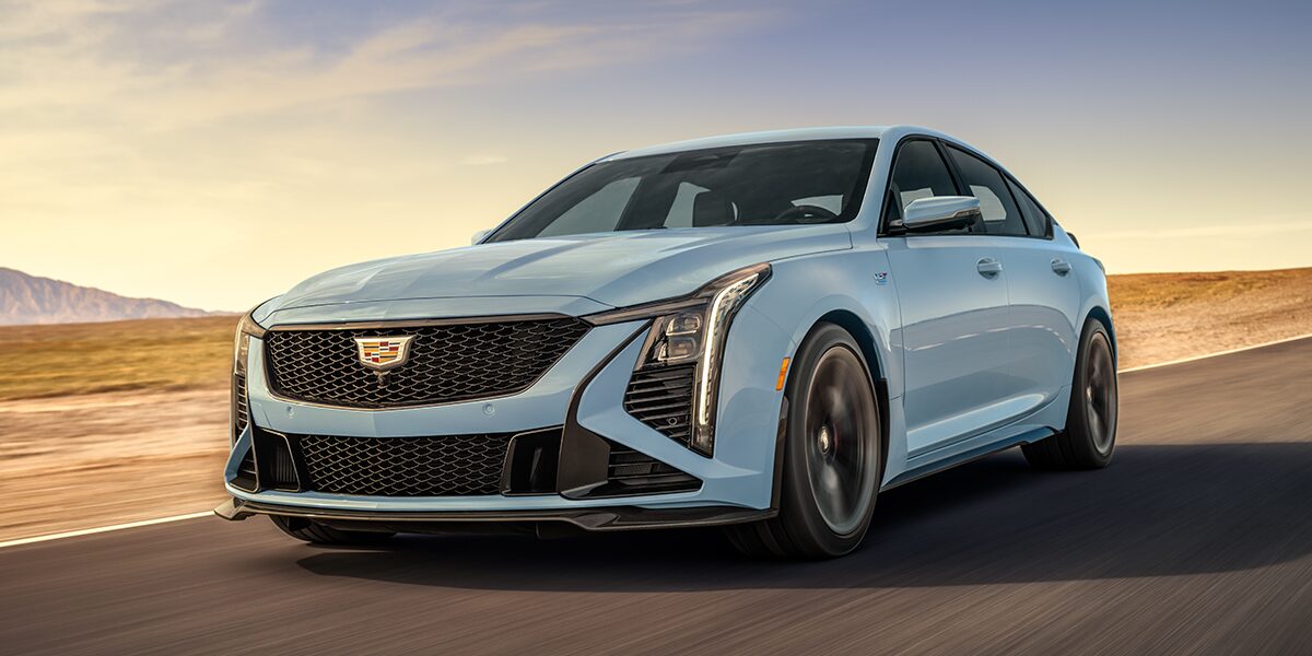 Low Three-Quarters View of a Light Blue 2025 Cadillac CT5-V Driving Down the Road Surrounded by Desert