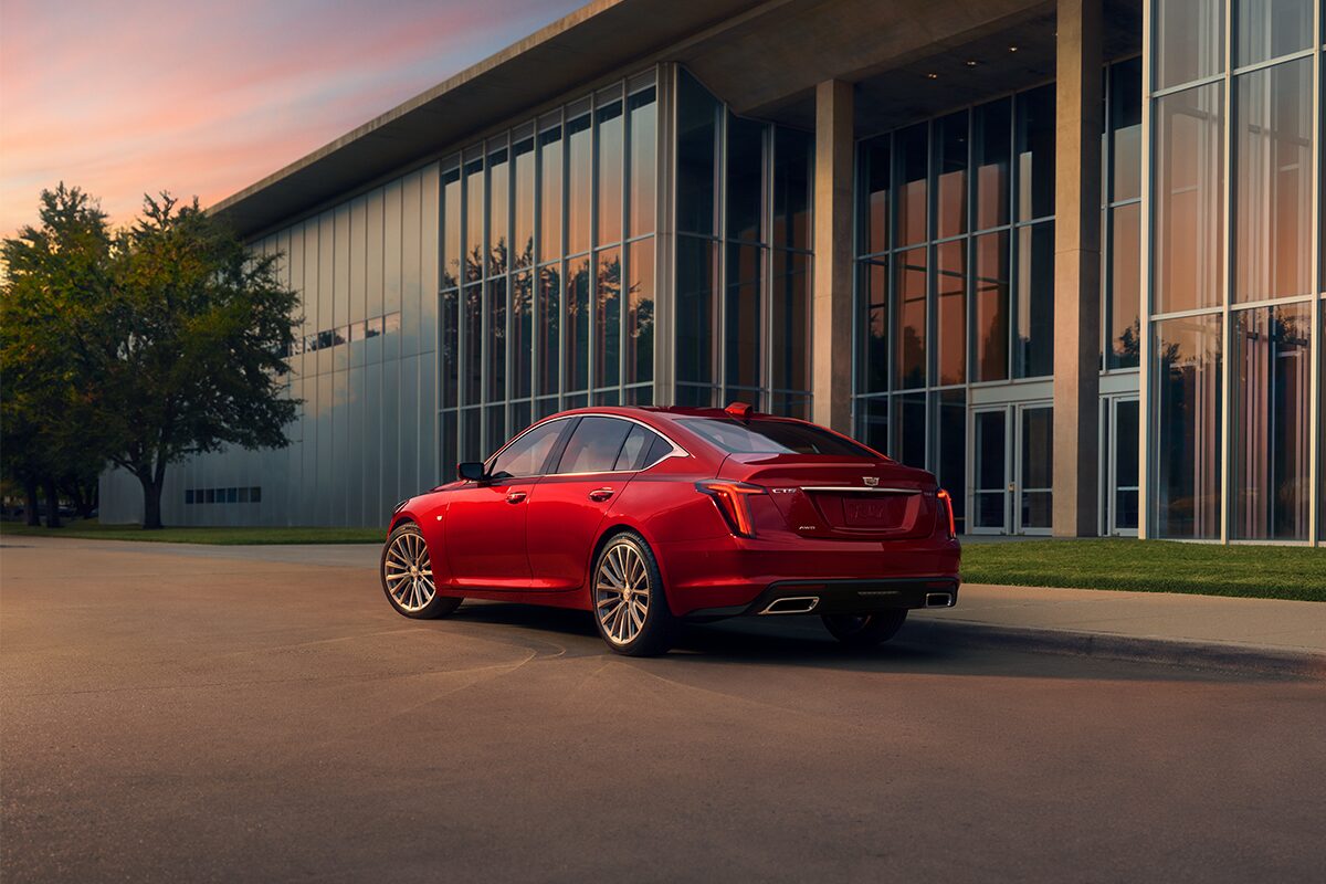 A Driver Side Rear View of a Red 2026 Cadillac Parked Near an Industrial Building