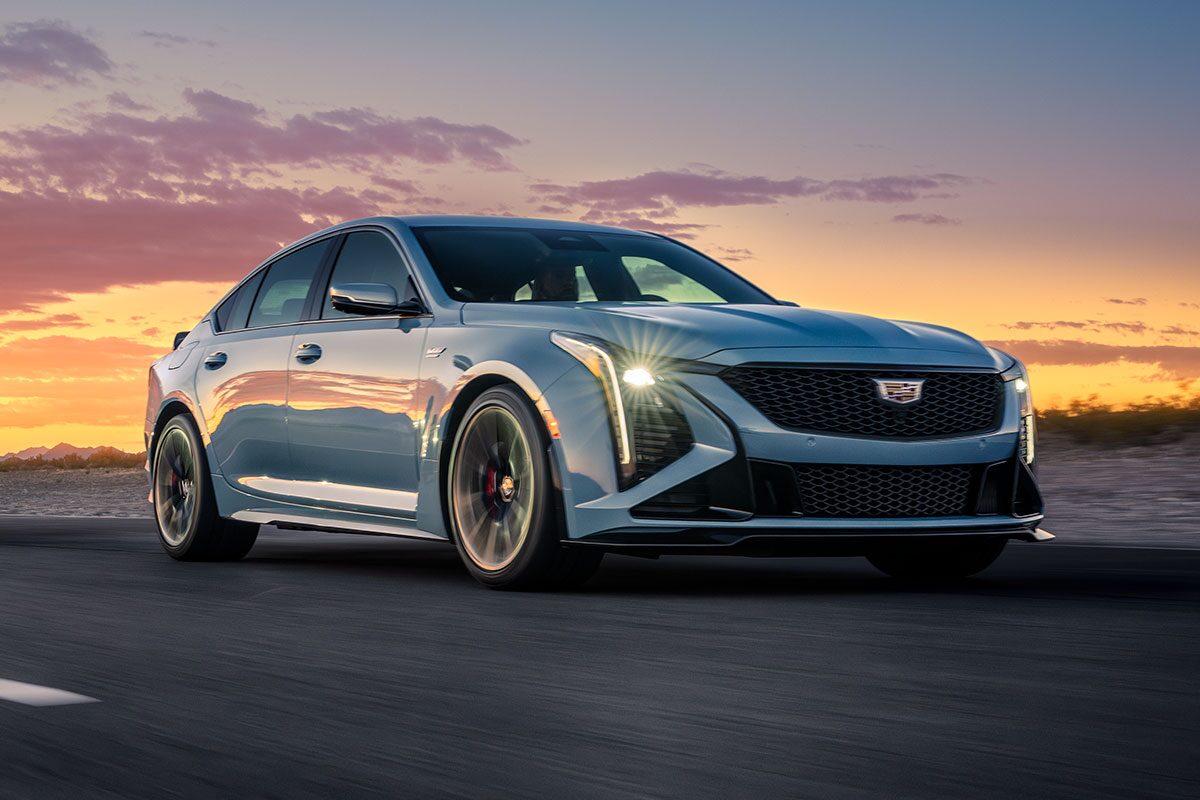 Two 2026 Cadillac CT5 V-Series Driving Down Winding Road with Stunning Sun Setting