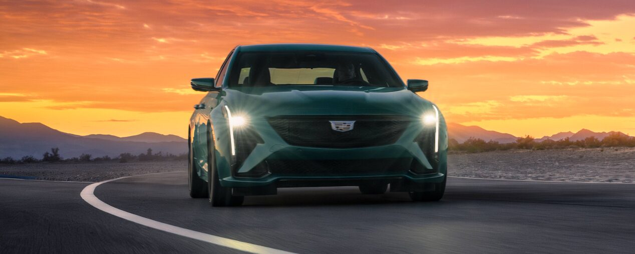 Front View of a Cadillac Performance V-Series Car Driving Down a Road with a Sunset Behind it.