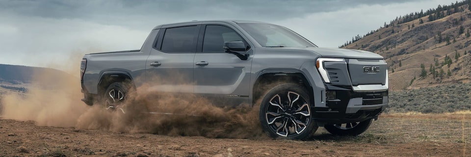 Side Profile View of the GMC Sierra EV Speeding Down a Dirt Road Kicking up Dust