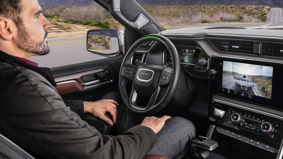 Profile View of a Man Using Super Cruise in his GMC While the Infotainment Screen Displays the Transparent Trailer View