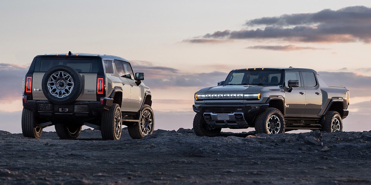 The GMC HUMMER EV SUV and the GMC HUMMER EV Pickup Truck Parked on Rough Terrain Over Looking a Beautiful Sunset Colored Sky