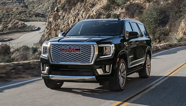 A Dark Gray GMC Yukon Denali SUV Driving on a Winding Mountain Road with Green Hills in the Background