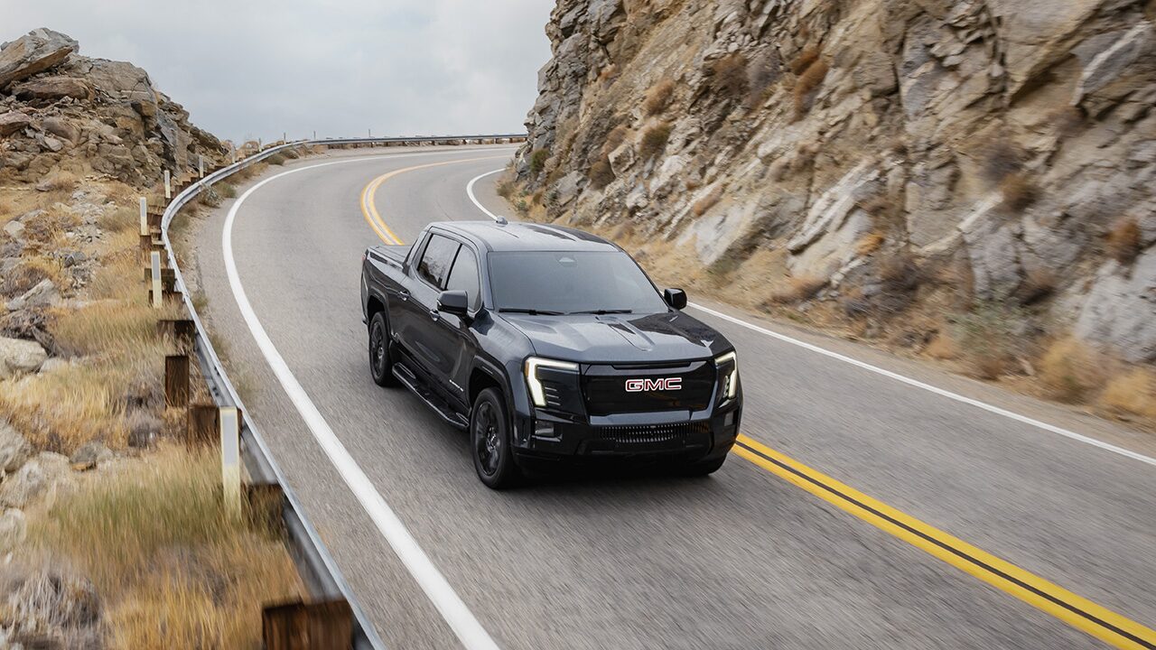 A Dark Gray GMC Sierra EV Pickup Truck Driving on a Winding Mountain Road with Rocky Cliffs
