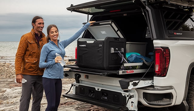 A Man and Woman Standing Next to an Open White GMC Truck Bed with a Dometic Cooler and Gear on a Slide-Out Tray