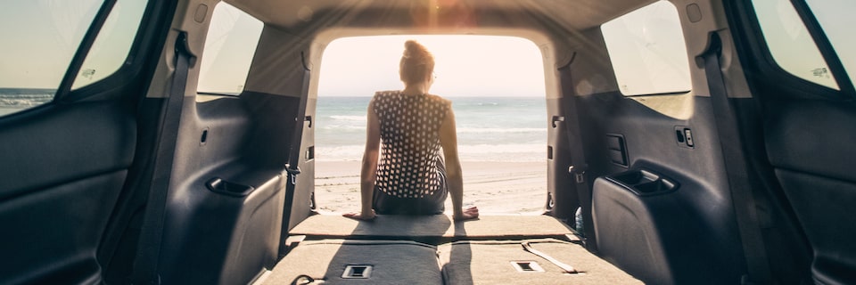 A Woman Sitting in the Cargo Space Area of a GMC SUV as she Looks out at the Beach View