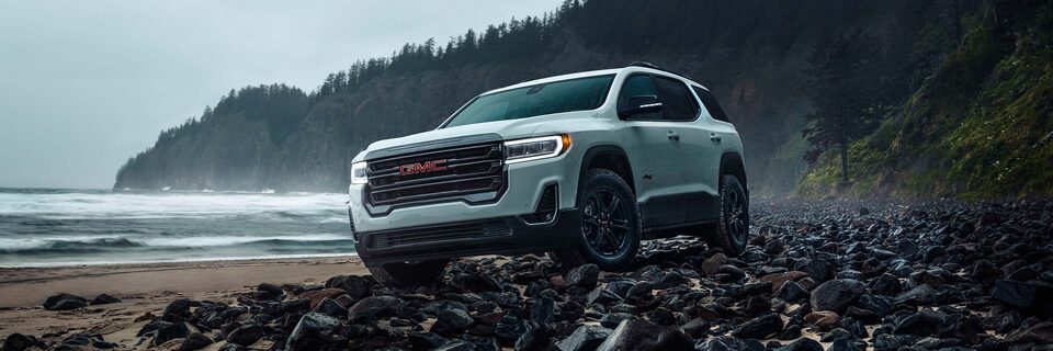 Three-Quarters View of a White GMC SUV Diving Over Rocks Next to a Beach