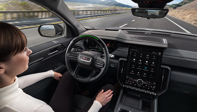 A Woman Driving a GMC Vehicle with Hands off the Steering Wheel on a Highway Showing Super Cruise Activated