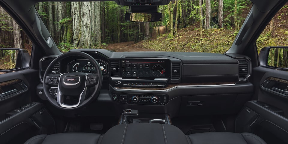 The Interior Dashboard and Steering Wheel of the GMC Sierra Truck with a Green Forest View Through the Windshield