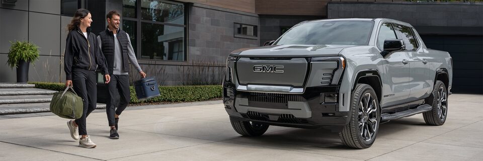 A couple leaving their house and walking to their Sierra EV pickup truck parked in the driveway.