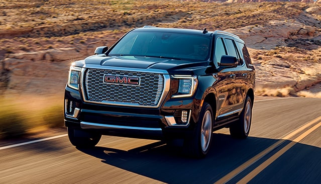 A Black GMC Yukon Denali SUV Driving on a Desert Road at Sunset With Mountains in the Background