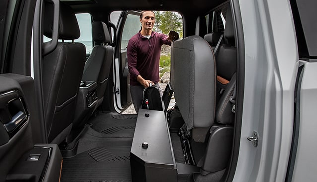 A Man Demonstrating the Spacious Interior of a GMC Truck with Folded Rear Seats and an Under-Seat Storage Compartment