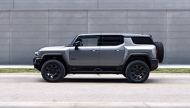 A Side View of a Gray GMC HUMMER EV SUV Parked Against a Modern Building Wall
