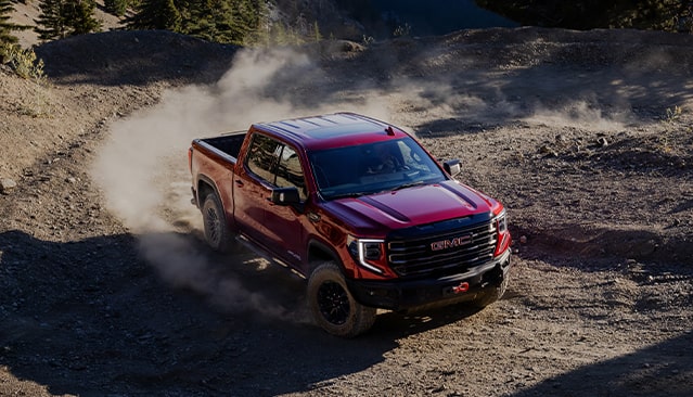A Red GMC Sierra AT4X Pickup Truck Driving Off-Road on a Dusty Trail With Mountains in the Background
