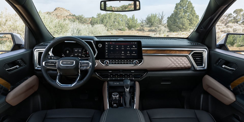 The Interior Dashboard and Steering Wheel of the GMC Canyon Truck with a Green Forest View Through the Windshield