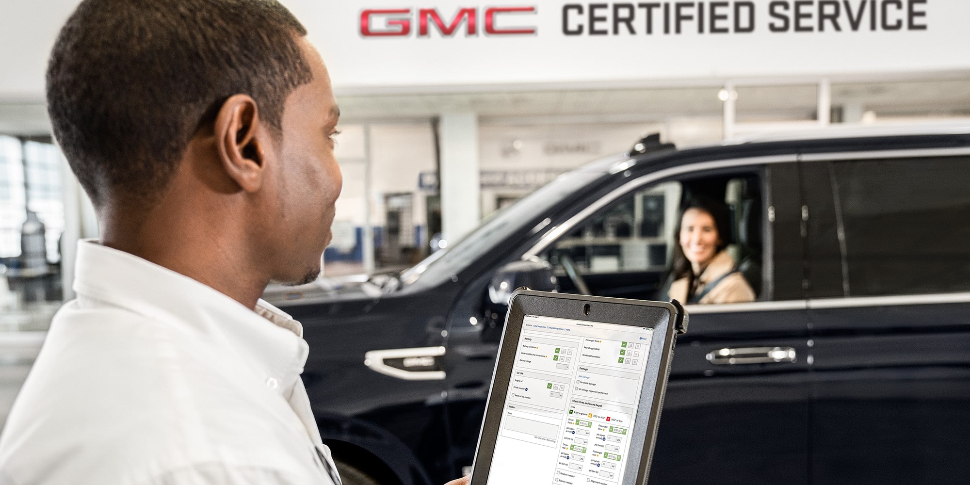 GMC Certified Service Representative Holding a Tablet Smiling at a Customer Sitting in Their Vehicle