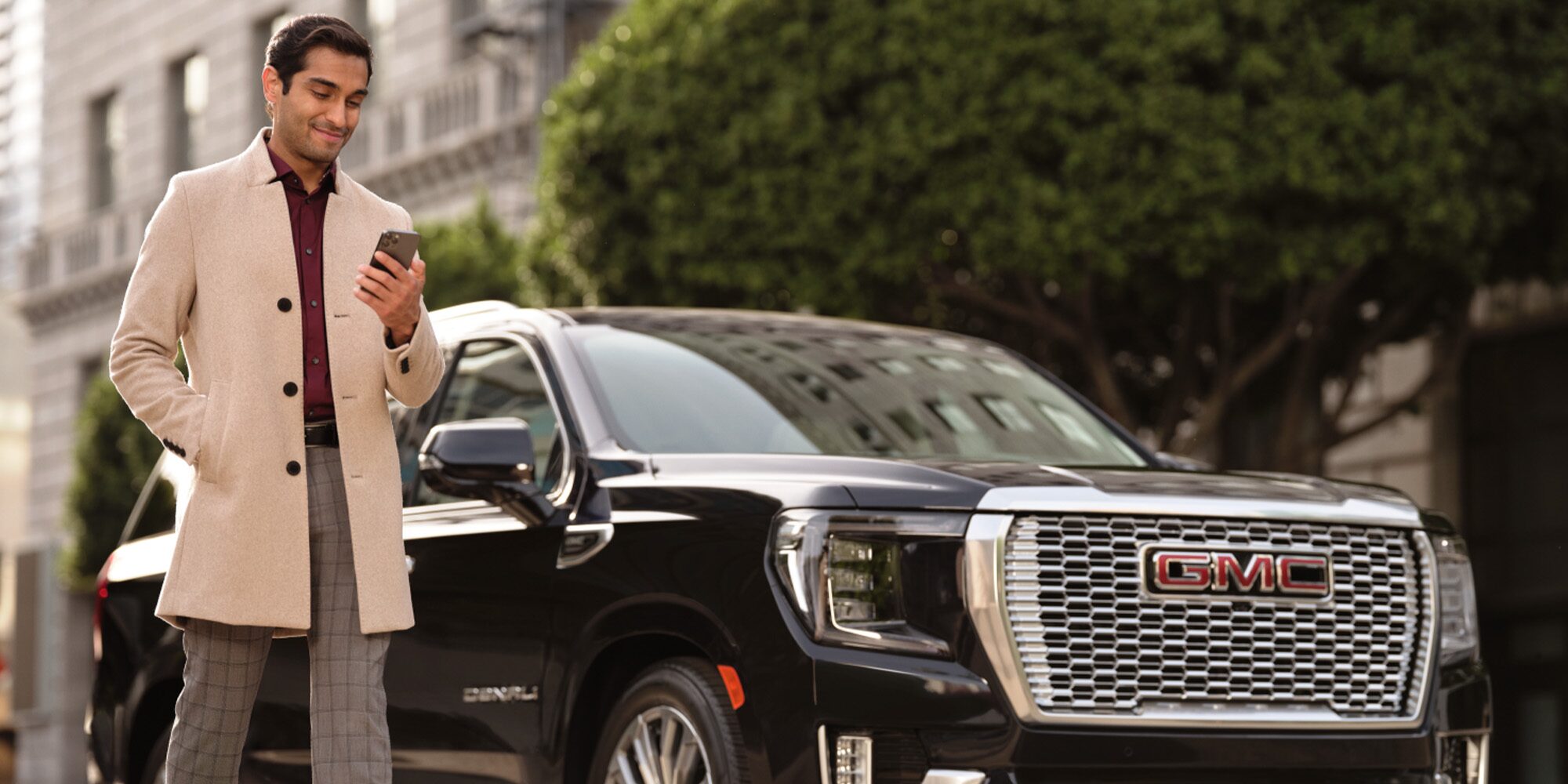 A Man Looking at His GMC Mobile App Next to His Black GMC Vehicle