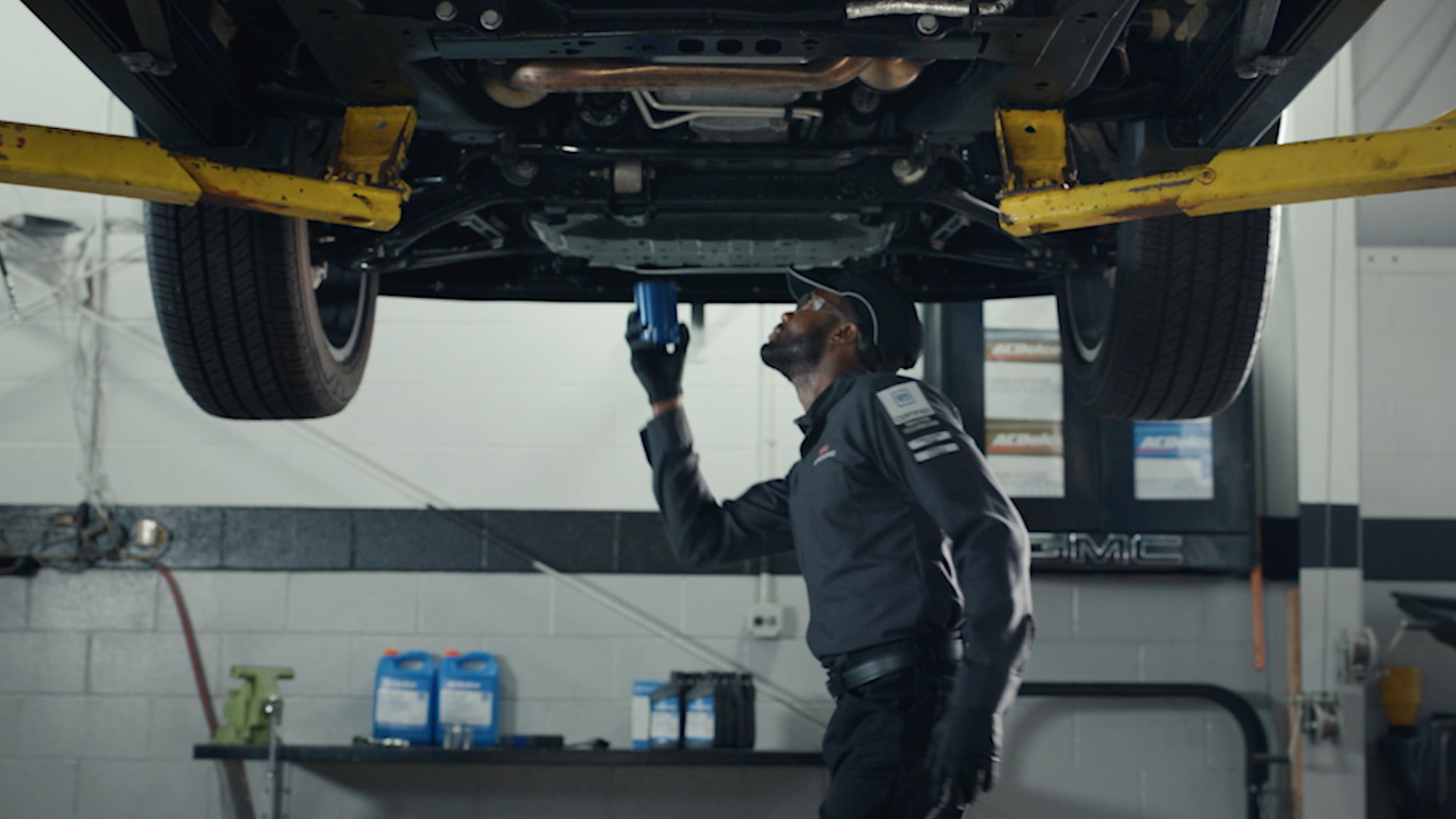 A GMC Service Technician Looking Under a Lifted Vehicle in a Service Garage.