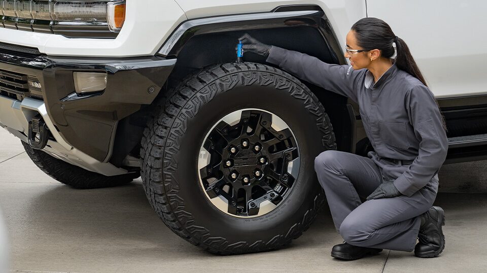 GMC Certified Service Technician Kneeling on the Ground Next to a Hummer EV Checking the Tire's Tread