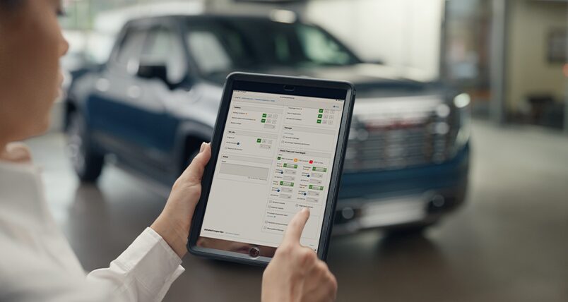 A Certified Technician Holding a Table in Front of a GMC Sierra EV with Details Displayed on the Tablet.