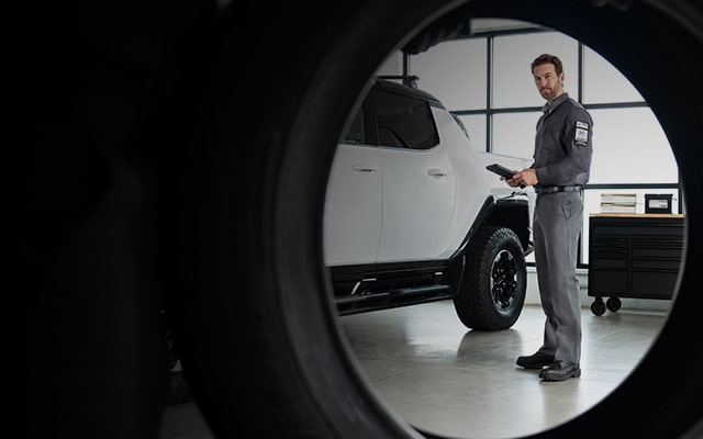 GMC Certified Service Technician Holding a Tablet Standing Next to a Hummer EV Truck