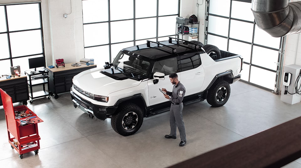 GMC Certified Service Technician Standing in a Service Bay Next to a GMC Hummer EV Truck