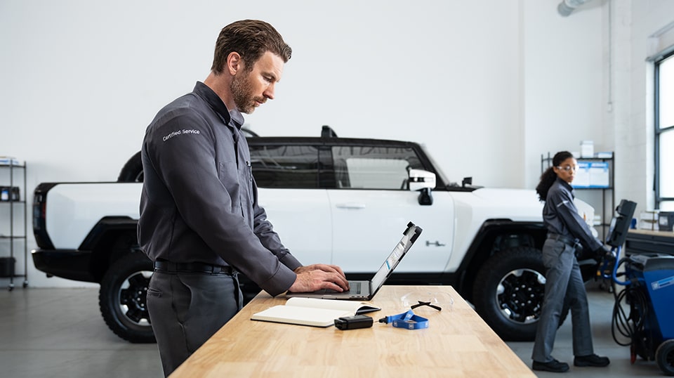 GMC Certified Service Technician Working on a Laptop with a GMC Hummer EV Truck Nearby